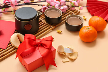 Gift box with fortune cookies, mandarins and cups of tea on beige background. New Year celebration