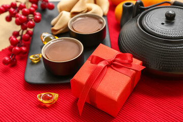 Gift box with teapot and cups of tea on red background. New Year celebration
