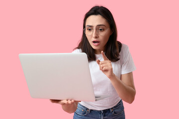 Confused young woman with laptop on pink background