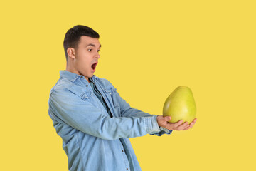 Shocked young man with pomelo on yellow background