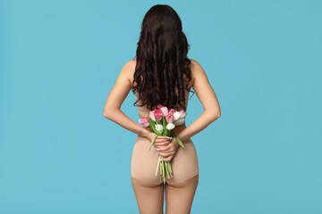 Beautiful young Asian woman in lingerie with bouquet of tulips on blue background, back view. International Women's Day - obrazy, fototapety, plakaty