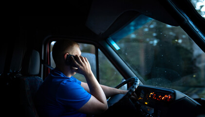 male truck driver is driving a truck and talking on the phone.
​