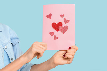 Young woman holding greeting card with hearts on blue background. Valentine's Day celebration