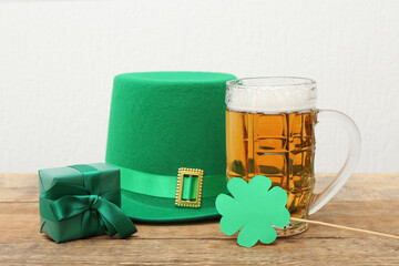 Mug of beer with leprechaun hat, gift box and paper clover on wooden table against white...