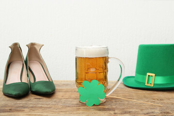 Mug of beer with paper clover, leprechaun hat and high heel shoes on wooden table against white...