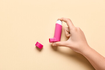 Child's hand with asthma inhaler on beige background