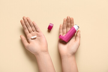 Child's hands with asthma inhaler and pill on beige background