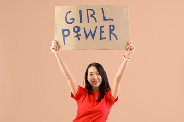 Beautiful young happy Asian woman holding paper with text GIRL POWER on beige background. Women...