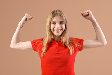 Beautiful young happy woman showing muscles on beige background. Women history month