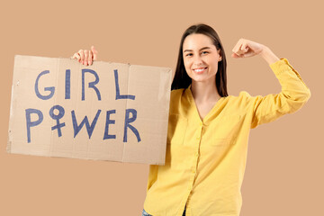 Beautiful young happy woman holding paper with text GIRL POWER and showing muscles on beige...