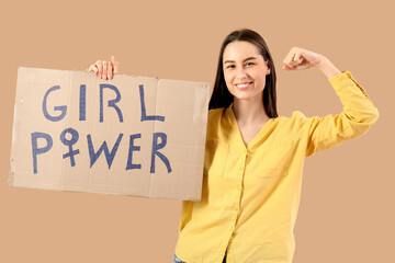 Beautiful young happy woman holding paper with text GIRL POWER and showing muscles on beige...