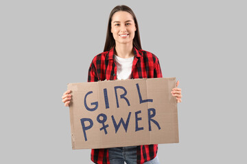 Beautiful young happy woman holding paper with text GIRL POWER on grey background. Women history...