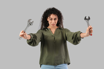 Beautiful young African-American woman with adjustable wrenches on grey background. Women history...