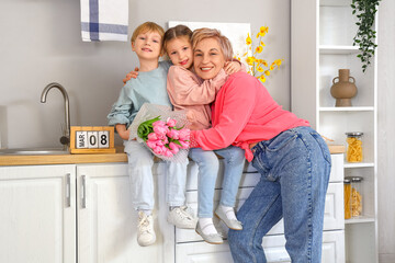 Little children and their grandmother with tulips hugging in kitchen. International Women's Day - obrazy, fototapety, plakaty