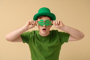 Shocked young man in leprechaun's hat with party glasses on beige background. St. Patrick's Day...