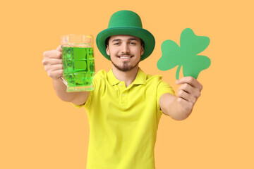 Happy young man in leprechaun's hat with mug of beer and clover on yellow background. St. Patrick's Day celebration