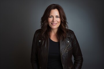 Beautiful middle aged woman in a leather jacket on a gray background - obrazy, fototapety, plakaty