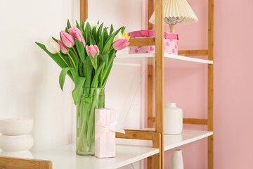 Vase with bouquet of tulips on shelving unit in living room, closeup. Valentine's Day celebration