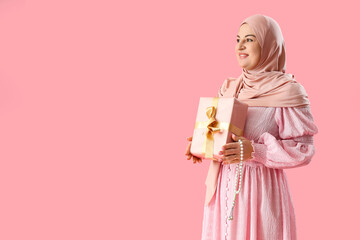 Mature Muslim woman with gift box on pink background. Ramadan celebration