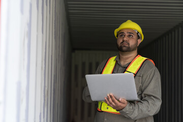 Male container yard worker working and checking into the container boxes before loading at commercial dock site. Male people worker inspecting container boxes from cargo freight ship