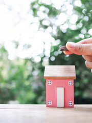 Close up hand putting coin with miniature house. The concept of saving money for house, Property investment, House mortgage, Real estate.