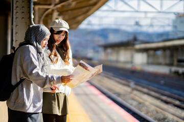 woman girl tourist Two Asian friends but different religions,They were looking at information about preparing to board the train at the train station,She is traveling in Japan. with fun, Japan travel  - obrazy, fototapety, plakaty