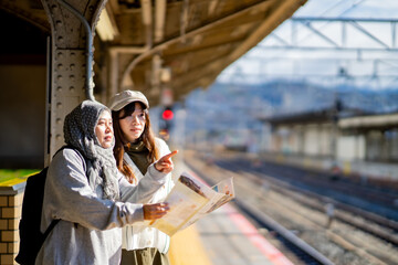 Fototapeta premium woman girl tourist Two Asian friends but different religions,They were looking at information about preparing to board the train at the train station,She is traveling in Japan. with fun, Japan travel 