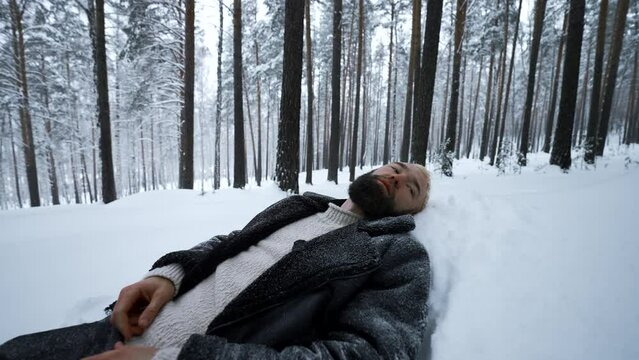 Man lies in snow in winter forest. Media. Tired man lies in snowdrift in winter forest. Depressive Stylish man lies in snow in winter forest