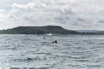 Local surfer paddling for riding waves on surfboard in reef break wave and backdrop of green hills, Indonesia, Asia