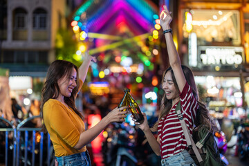 Asian woman friends hold bottle of beer, having party infront of bar.