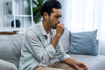 Asian handsome male feeling unwell and sick, coughing in living room. 