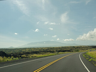 Driving to distant Mauna Kea volcano by Saddle road with black lava rock volcanic landscape on roadsides on beautiful sunny day, Big Island of Hawaii