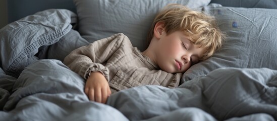 Blond boy sleeping on gray bed linen, dreaming on a big bed with soft cushions.