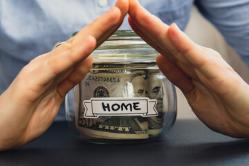 Unrecognizable woman holding Saving Money In Glass Jar filled with Dollars banknotes. HOME...