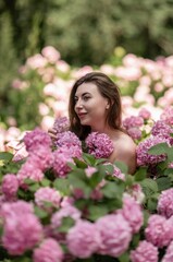 Naklejka premium Hydrangeas Happy woman in pink dress amid hydrangeas. Large pink hydrangea caps surround woman. Sunny outdoor setting. Showcasing happy woman amid hydrangea bloom.