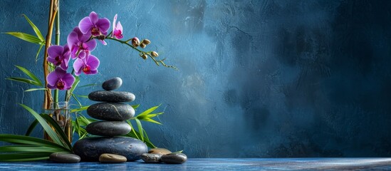 Blue background still life featuring bamboo plant, orchid, and stones.