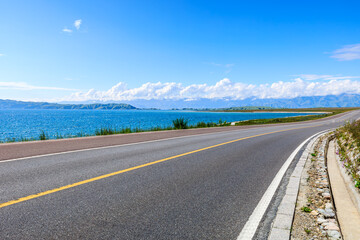 Asphalt highway road and blue lake with mountain nature landscape under blue sky