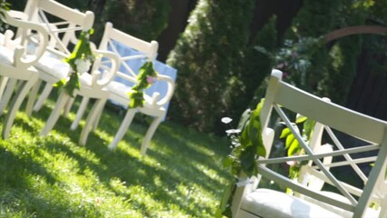 Wedding decor for outdoor cerimony. Wedding arch and chairs for guests in white color on green grass in sunny weather. Backyard wedding venue. Furniture and decoration for outside wedding party. 