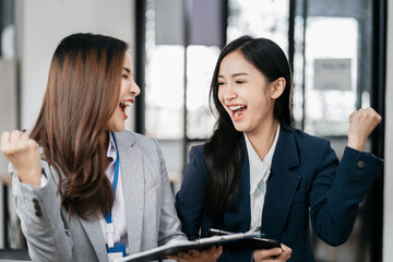 Asian business woman are excited business success with inspiration from their excellent financial results that are happy working in a modern office on a computer.