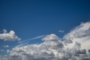 Vast blue sky with various white cumulus clouds illuminated by daylight