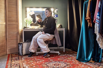 Full length portrait of female mime performer sitting by mirror backstage preparing for show in theater, copy space