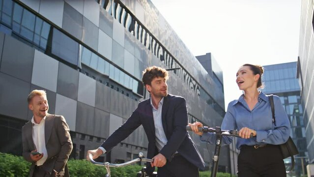 Joyful coworkers going street with eco scooter bicycle. Happy business people