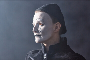 Dramatic headshot portrait of mime artist standing on stage in spotlight and looking away with sad...