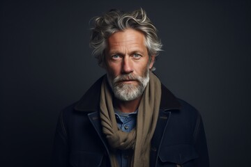 Portrait of a handsome senior man with gray hair and beard wearing a blue coat and scarf.