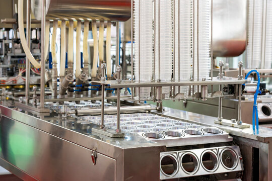 Close up row transparent plastic cup set on feeding unit of automatic continuous filling and sealing machine for food beverage or cream sauce packing etc. in industrial