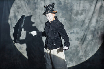 Waist up portrait of classic mime performer acting on stage in spotlight with umbrella, copy space