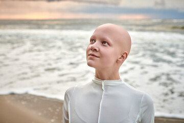 Close up portrait of young hairless girl with alopecia in white futuristic costume on sea background, bald pretty teenage girl showcasing unique beauty and identity with pride, unusual alien girl