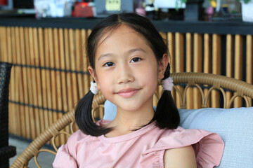 Close up portrait of Asian young girl child age about 9 years old lying on chair and looking camera. - obrazy, fototapety, plakaty