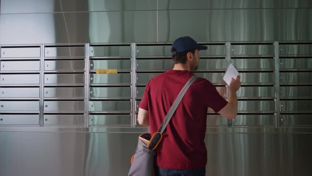 Postman putting letters mailbox in apartment building. Guy working checking post
