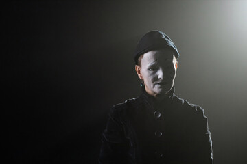 Minimal portrait of sad mime standing on stage in contour lighting against black background, copy...